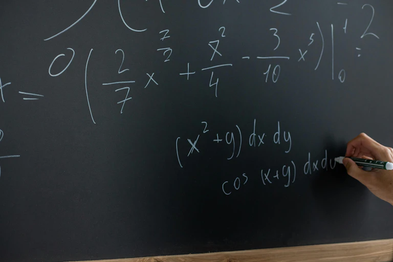 A hand writes equations on a board.