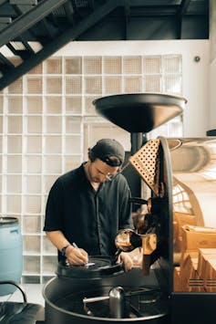 man stands over a coffee roaster and fills in a clipboard