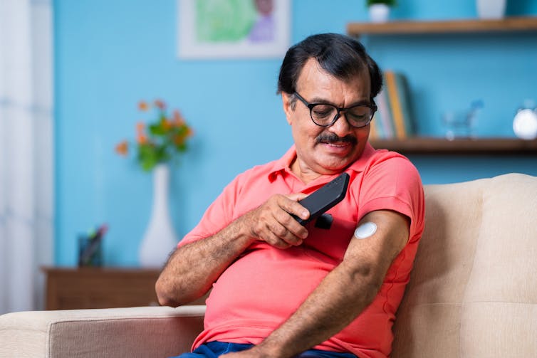 A man checking the glucose monitor on his arm.