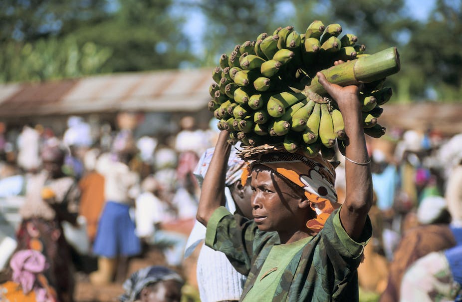 Woman with a large bunch of bananas on her head, in what appears to be a marketplace