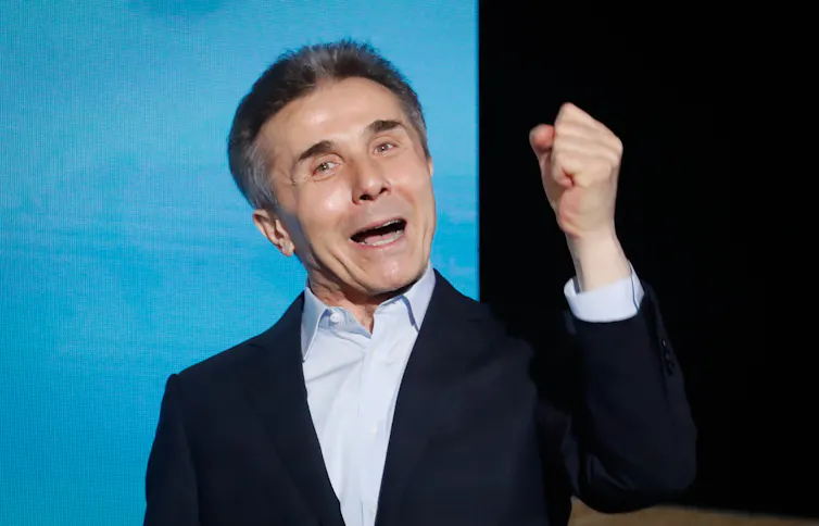 A close-up of a man raising his fist and cheering against a blue and black background.