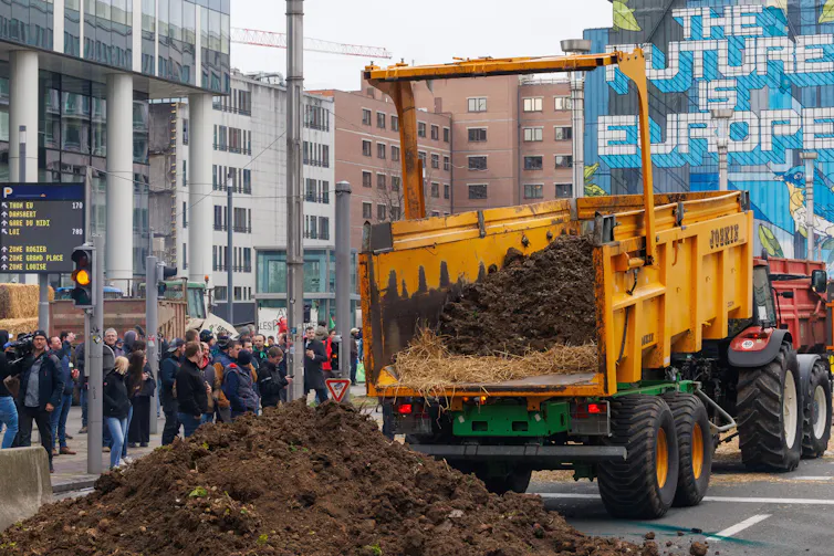 Farmers drop earth between flares lit by protesters on the side of an Agriculture and Fisheries Council in Brussels, Belgium, 26 March 2024.
