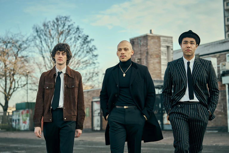 Three young men walking towards the camera looking sombre.