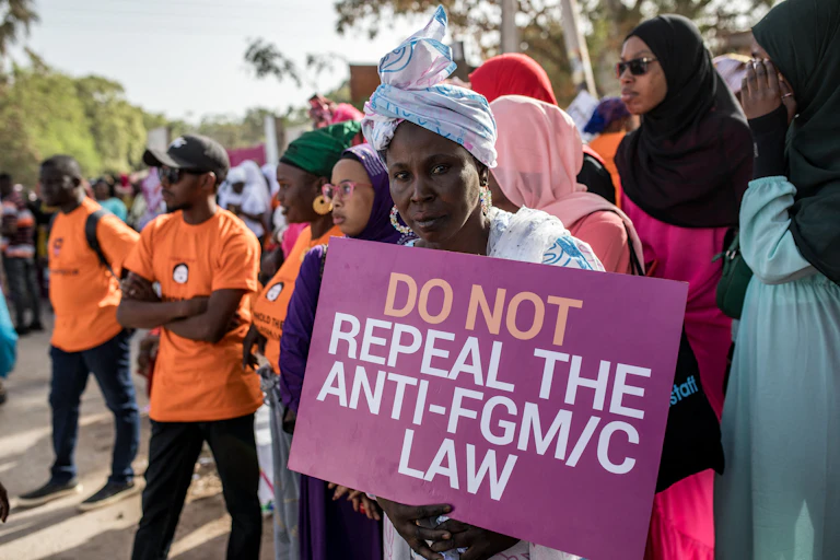 A woman holds a poster, standing in a group of women and men outdoors
