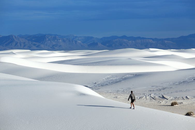 Man walks on white dunes, mountains in background