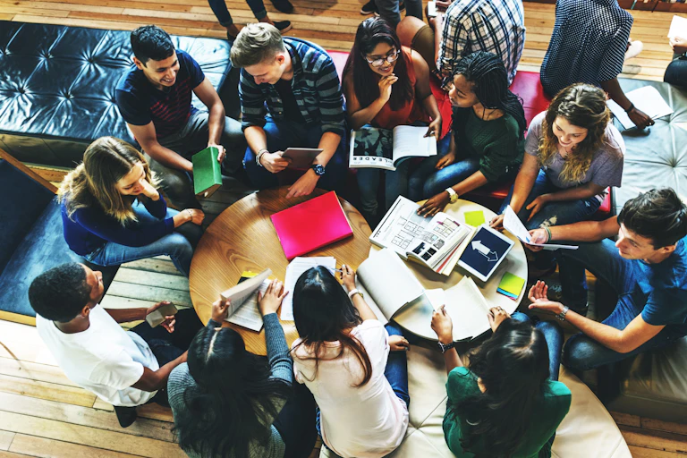 Students seen sitting around a table in discussion with books and learning materials.