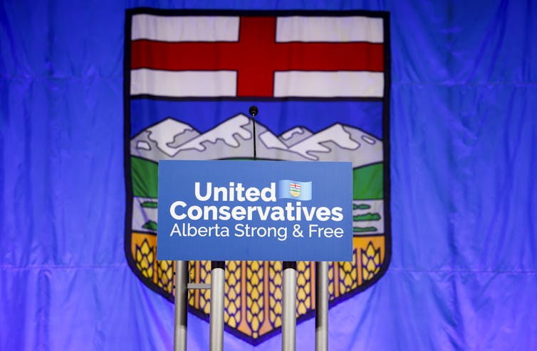 A sign saying United Conservatives in front of a flag with a red cross and mountains.