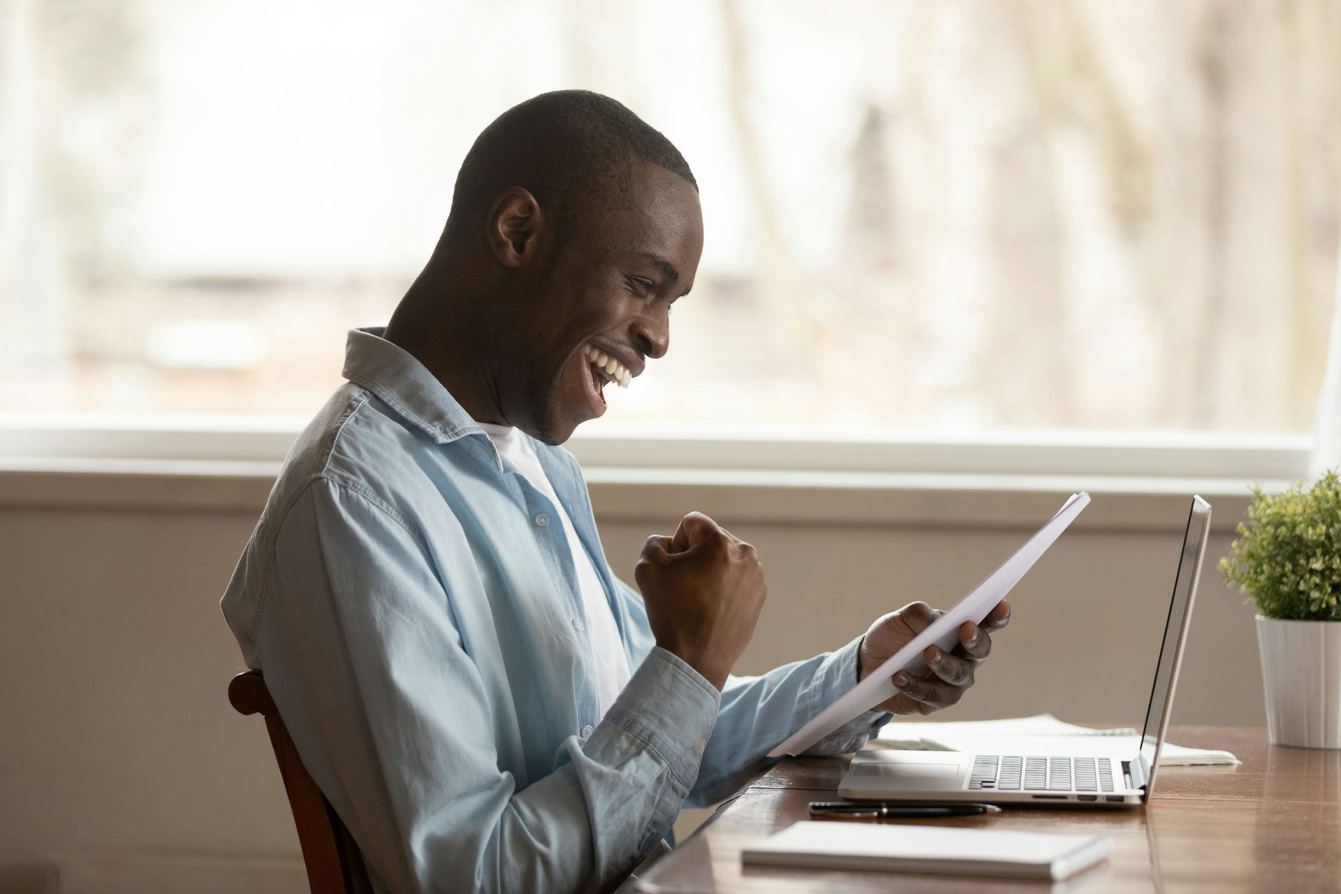 A student seen sitting at a keyboard celebrating holding a piece of paper.