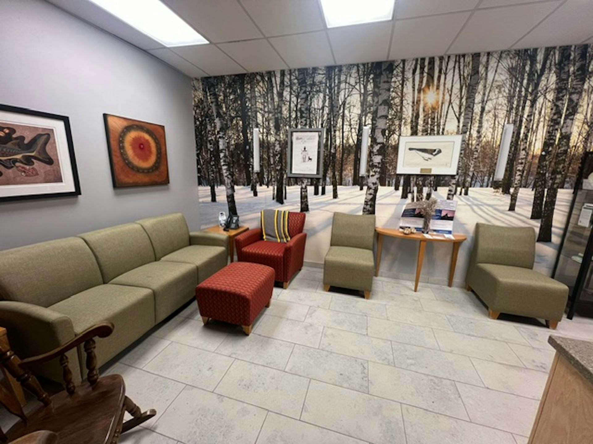 A room with comfortable chairs, artwork and an image of trees and snow covering a full wall