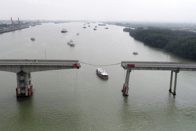 photo of ships and boats sail on a river. a bridge with a section missing from the middle is in the foreground