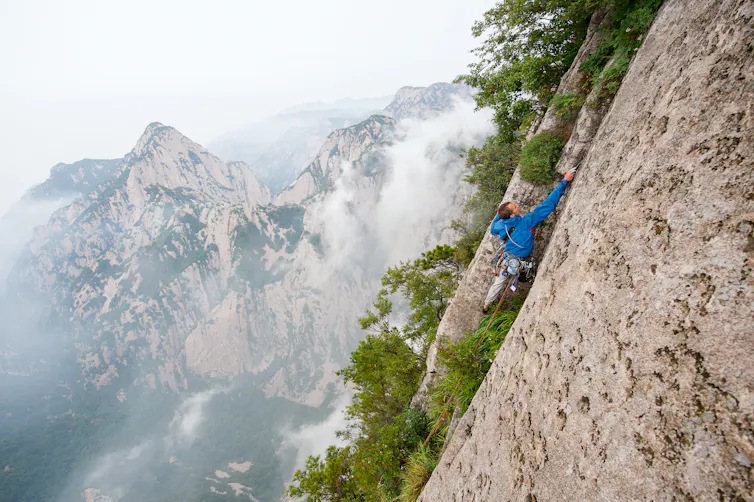 A man in blue climbing a sheer mountain side.