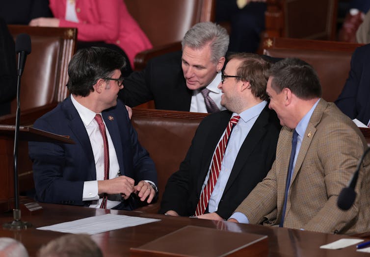 Four men in suits talking while sitting down.