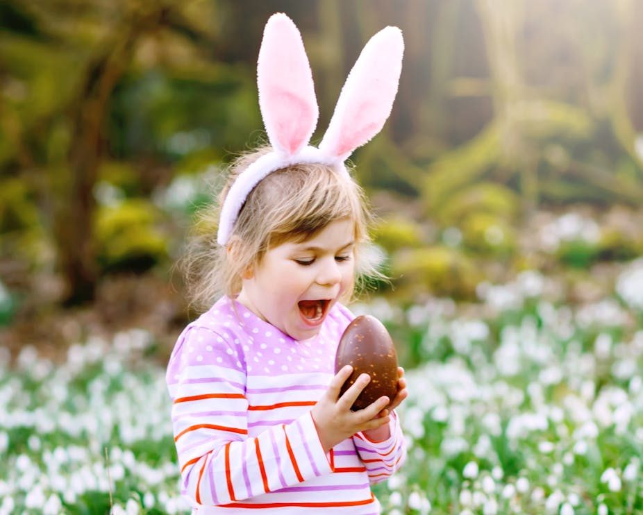 Little girl in bunny ears about to bite into an Easter egg