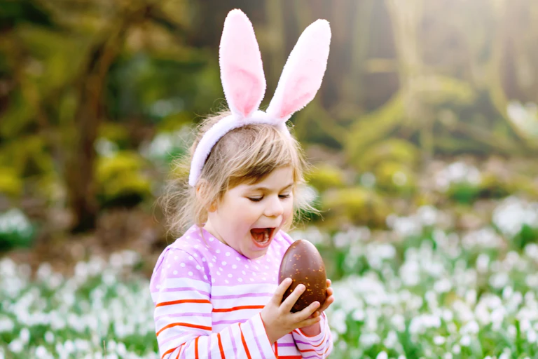 Little girl in bunny ears about to bite into an Easter egg