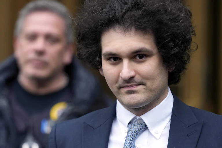 man with bushy hair and blue suit stairs ahead in front of another man in a windbreaker