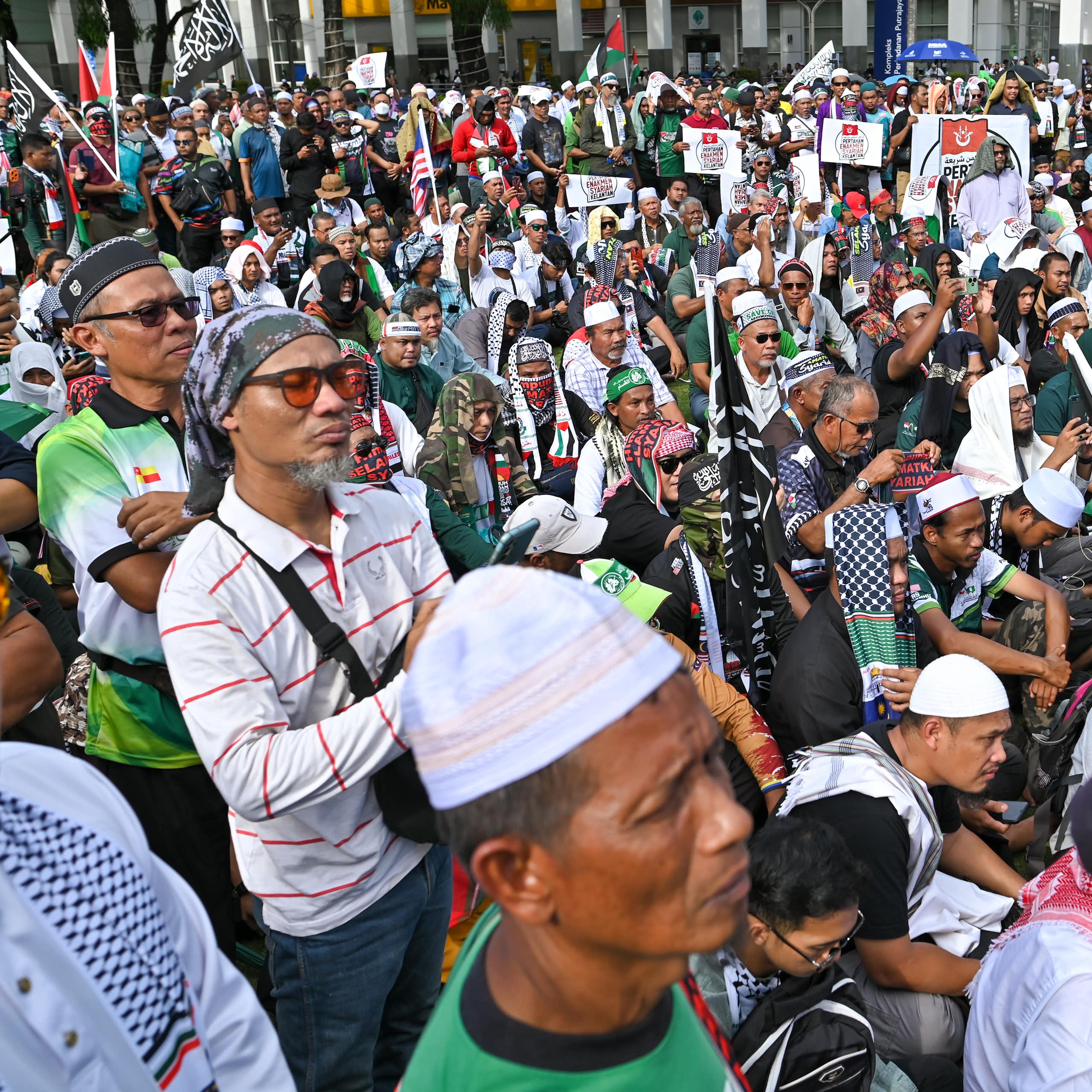 Un grupo de manifestantes, muchos de ellos con tocados islámicos, permanecen de pie y sentados.