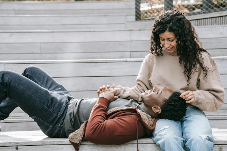 A woman sitting on a bench and a man lying on the bench with his head on her lap