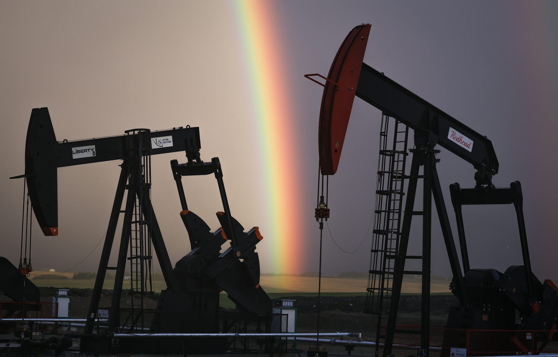 Pumpjacks seen against a dark, purplish sky split in half by a rainbow