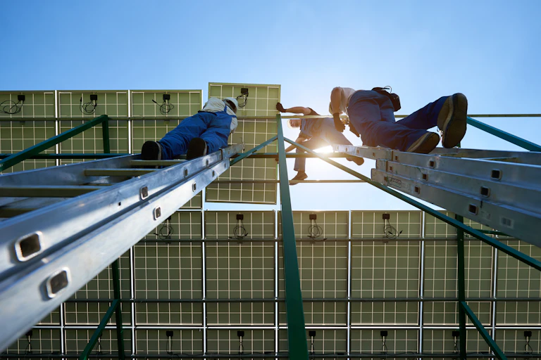 An upwards shot of workers in overalls installing solar panels on a roof