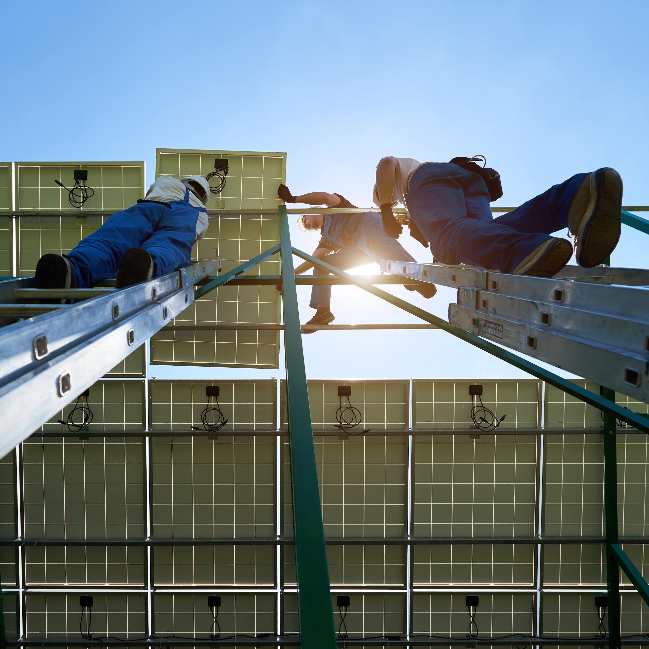 An upwards shot of workers in overalls installing solar panels on a roof