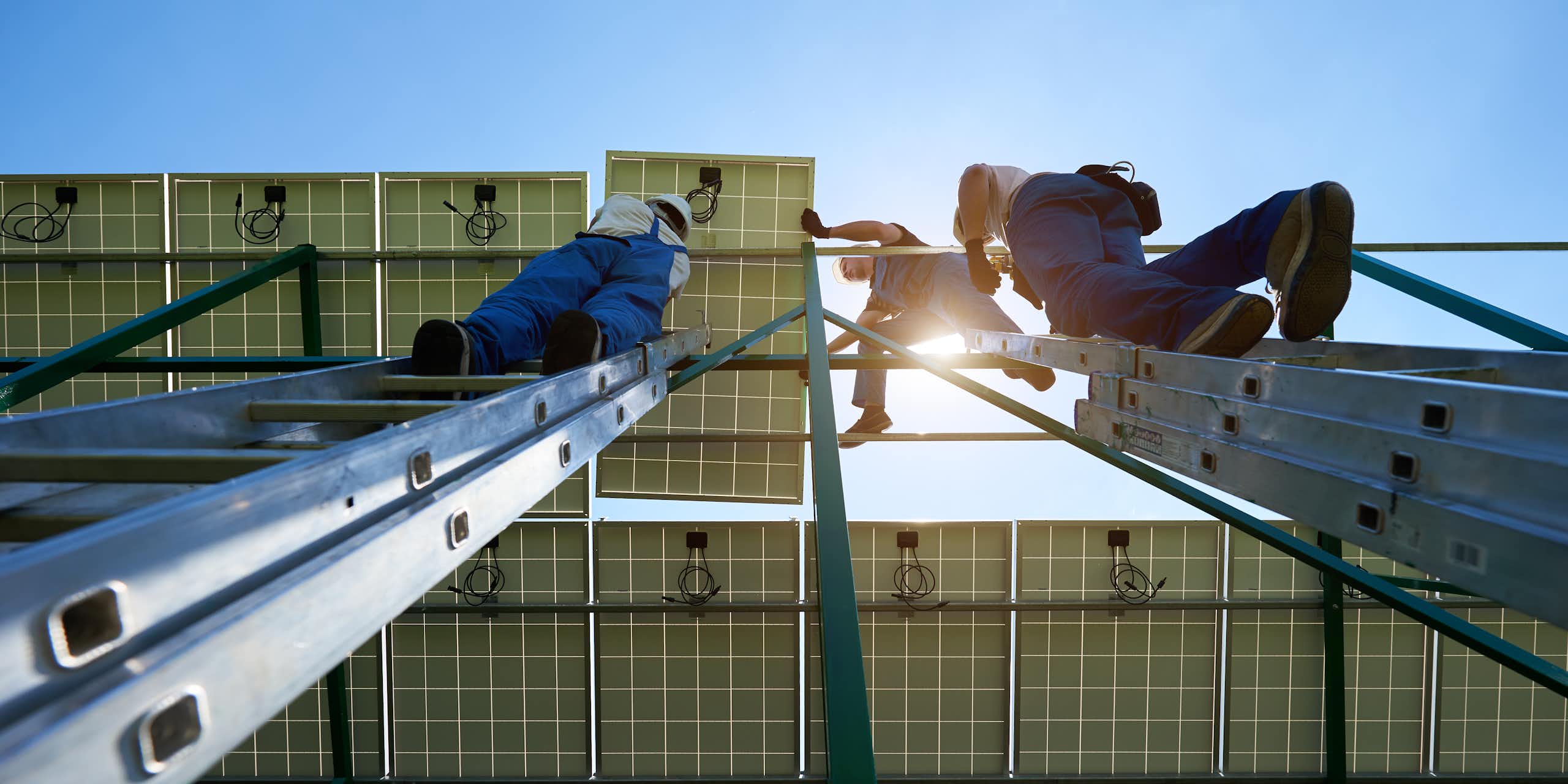 An upwards shot of workers in overalls installing solar panels on a roof