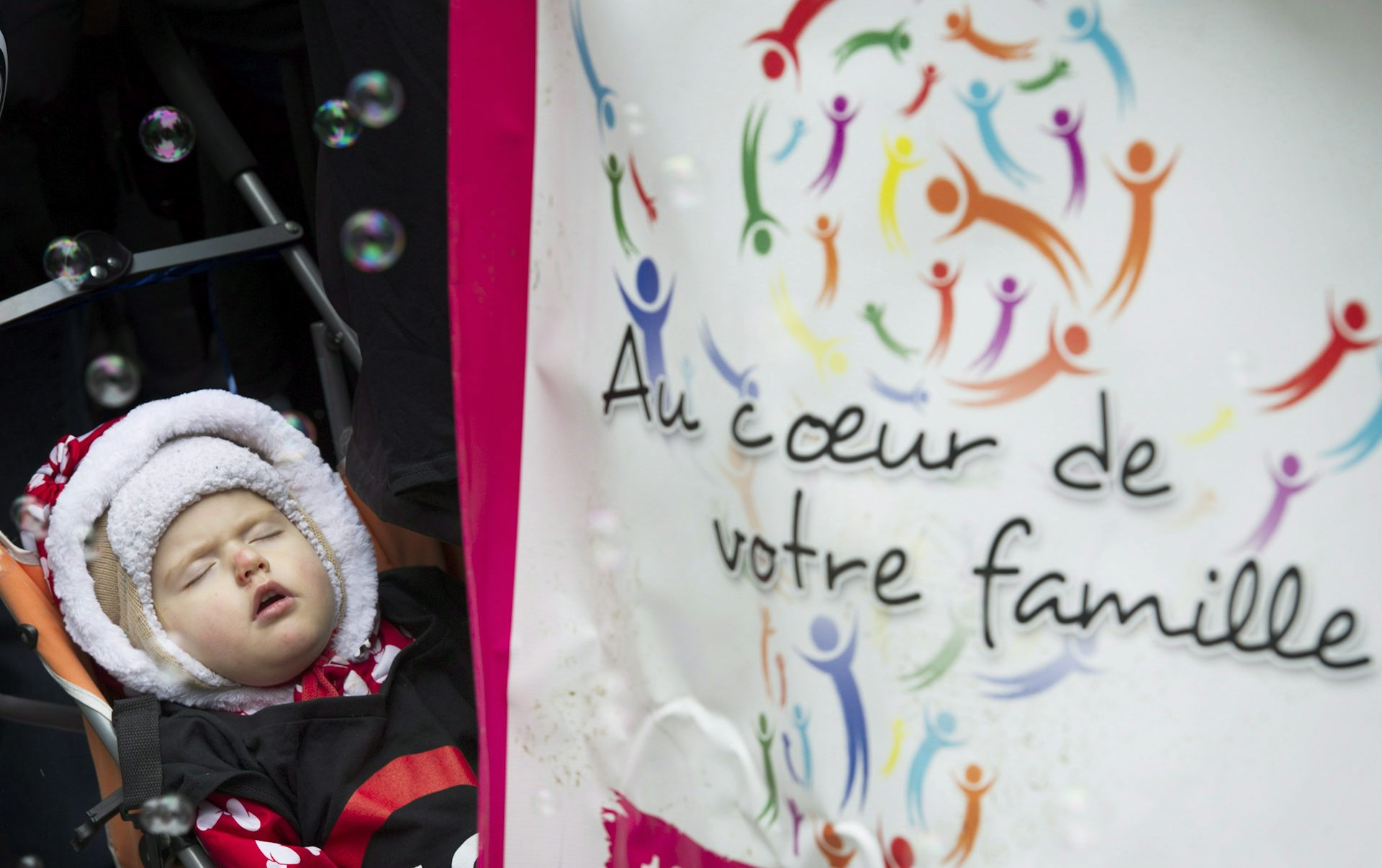 A child in a stroller sleeping beside a sign that says 'at the heart of your family' in French.
