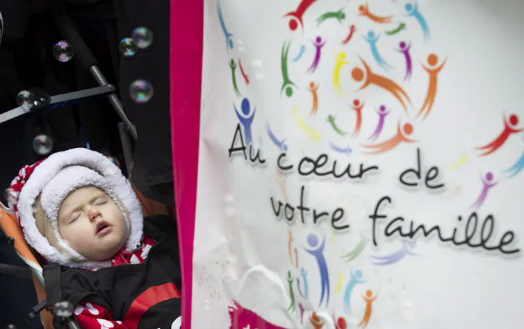 A child in a stroller sleeping beside a sign that says 'at the heart of your family' in French.