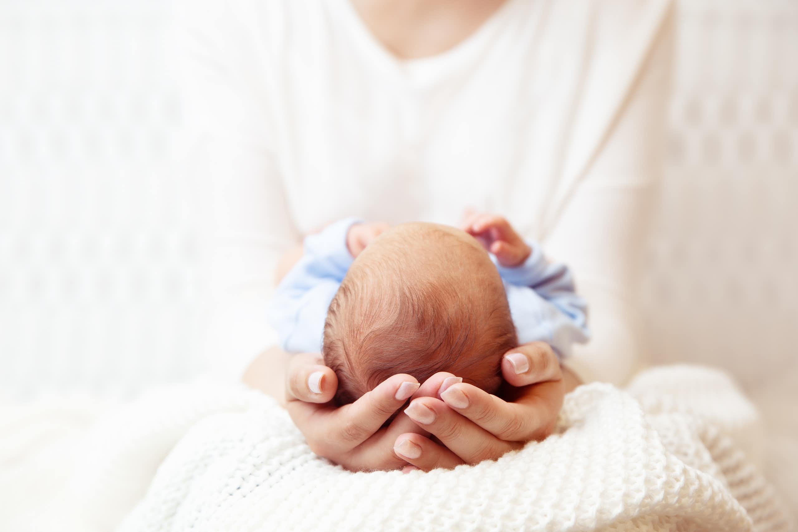 Une femme tient entre ses mains un nouveau-né dont on ne voit que le haut de la tête.