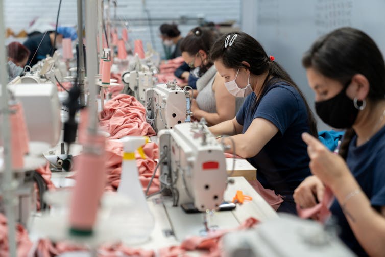 Row of people wearing masks sewing clothes in a textile factory