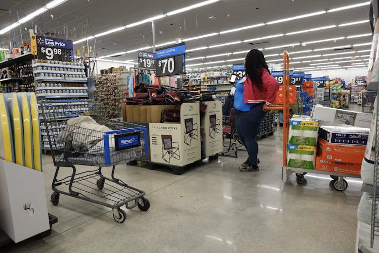 A worker stands next to a hand truck loaded with products at a Walmart store