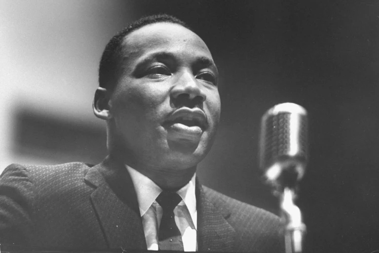 A close-up, black and white photograph of a man in a suit speaking into a microphone.