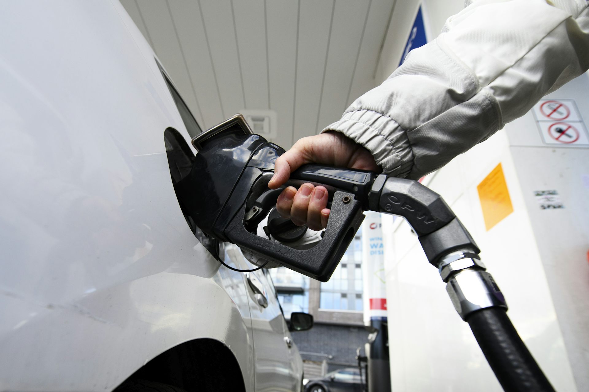 A person's hand and forearm is seen as they pump gas into a white vehicle.