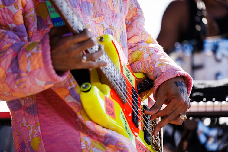 Close up of musician wearing bright colors playing a yellow and red bass guitar