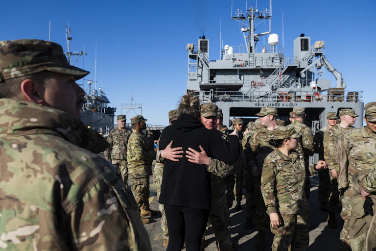 Men and women in fatigues embrace on a military ship.