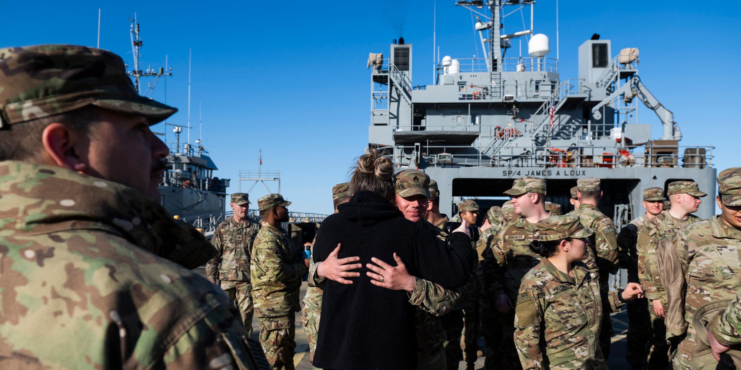 Men and women in fatigues embrace on a military ship.