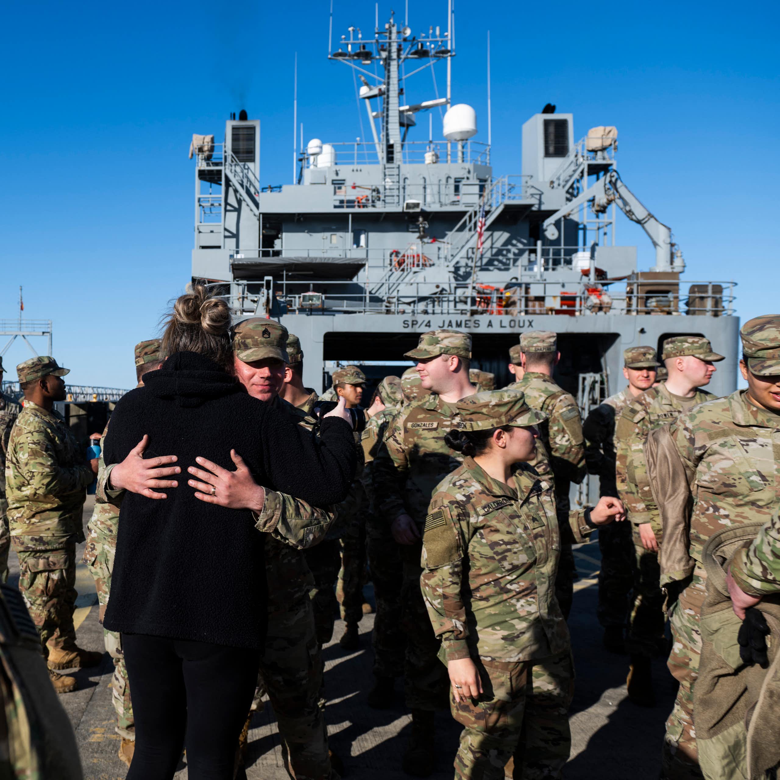Men and women in fatigues embrace on a military ship.