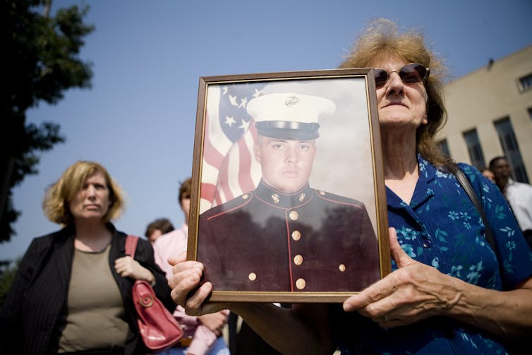 A woman holds portrait of man in uniform.
