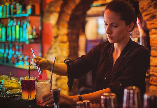 Female bar attendant adds cherry to a cocktail
