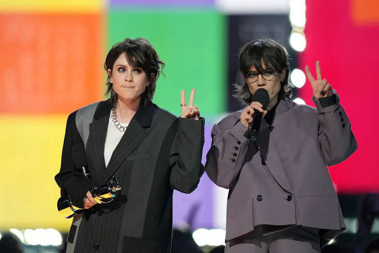 Two people in formal suits, one holding an award statue and one holding an award.