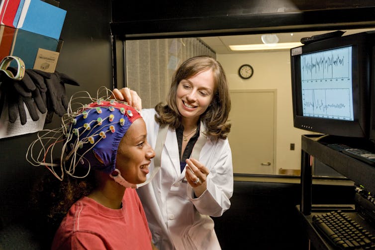 A female doctor adjusts electrodes on the head of a female patient.