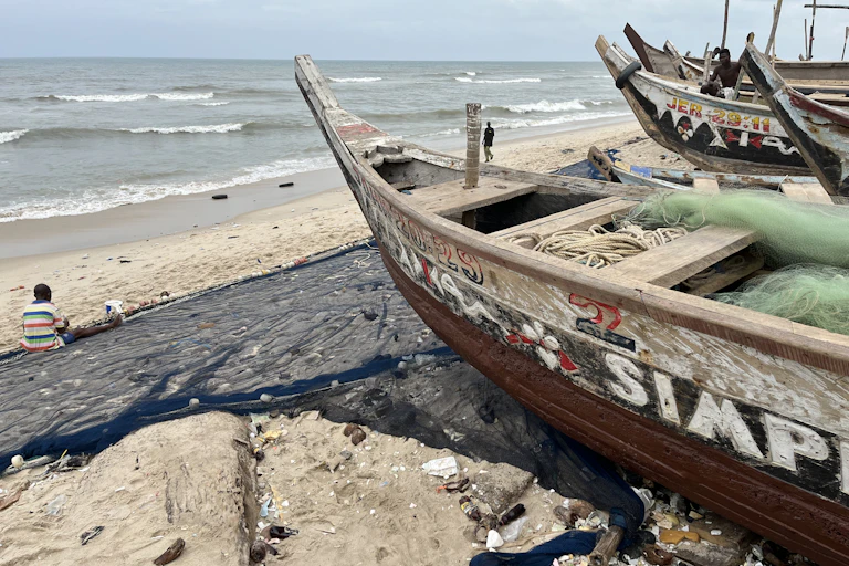 A fisherman sits on the sand at the beach to fix his net