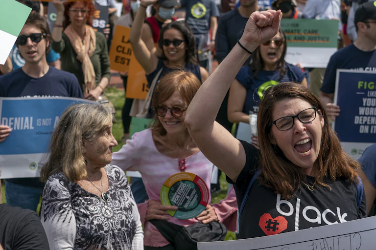 Middle-age activists hold signs and shout. Two older women are also there, along with some younger people in the background. All are smiling.