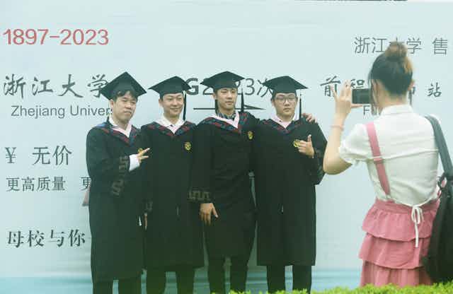 woman taking photo of four Chinese grads wearing robes and hats