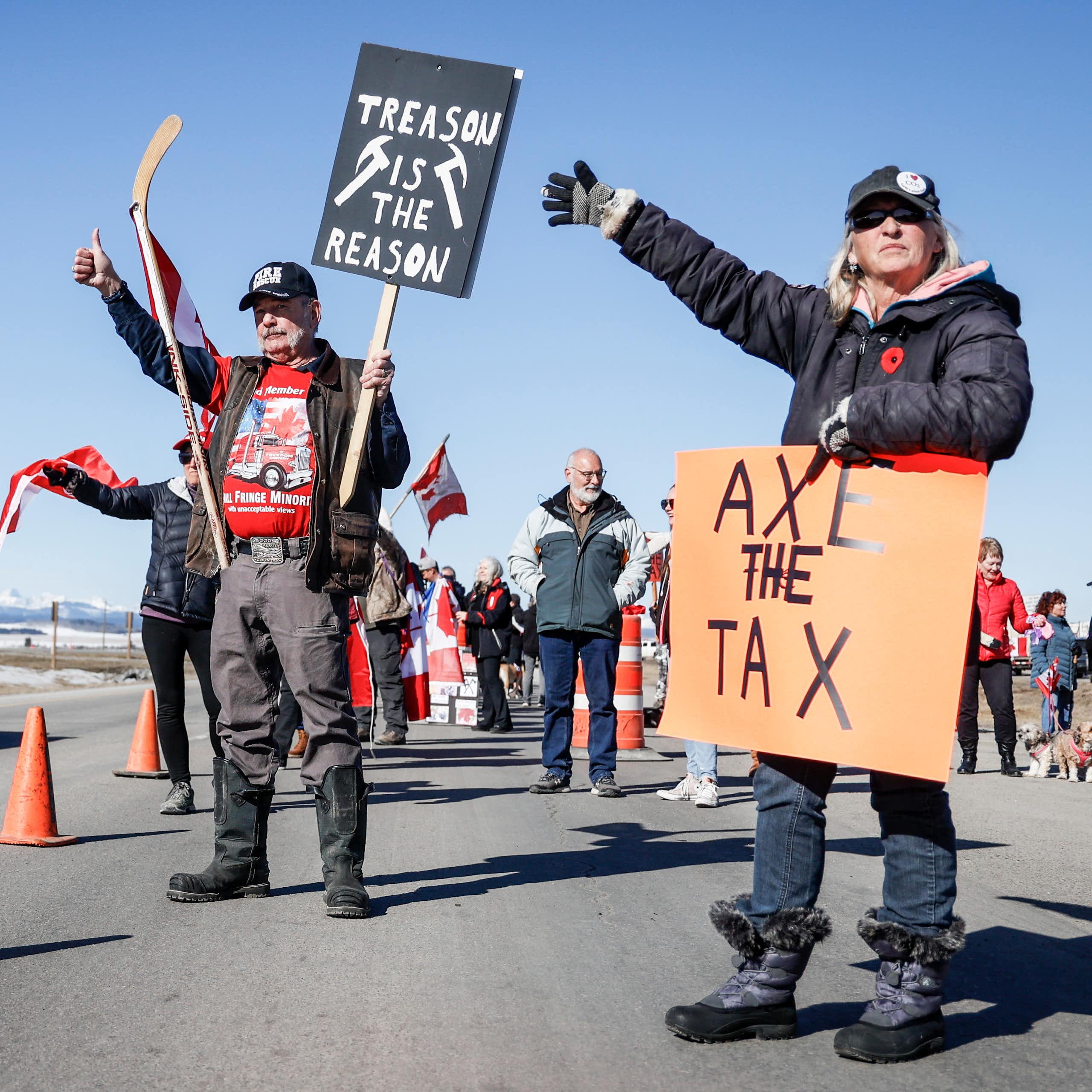People stand at the side of a highway. One carries a sign that reads Axe the Tax.