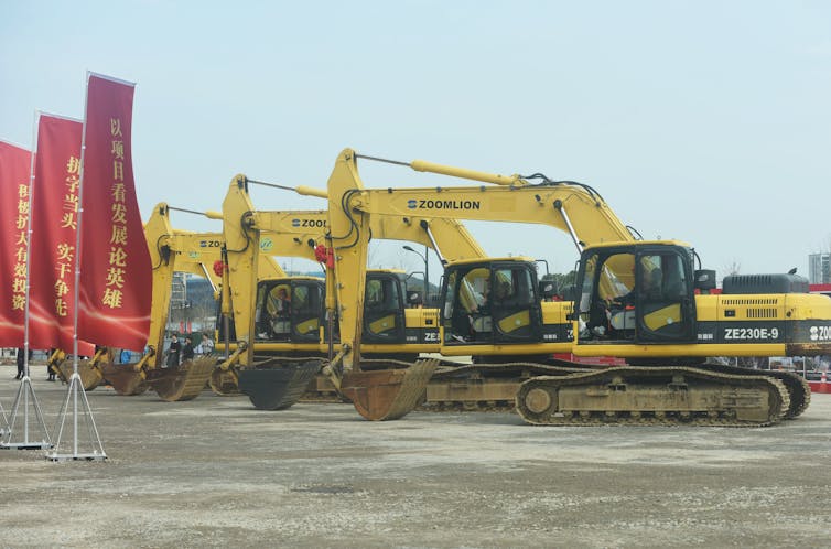 multiple yellow excavators posed next to red flags with Chinese lettering