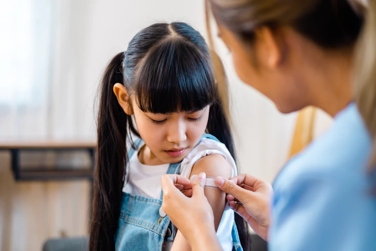 A girl has a bandaid put on her upper arm.