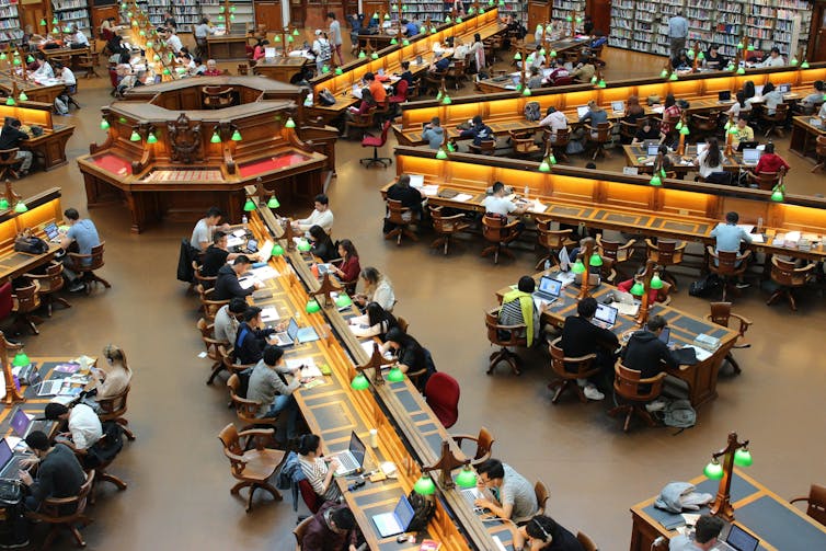 People seated at desks, working and reading in a public library.