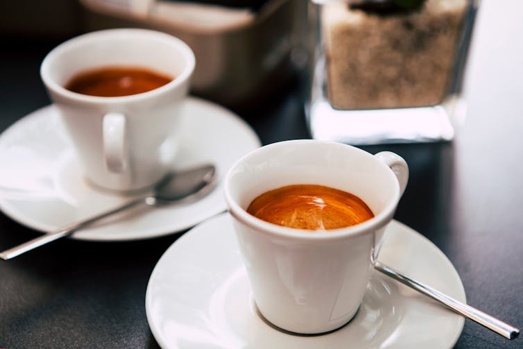 Two small coffee cups with espresso in them are laid on saucers.
