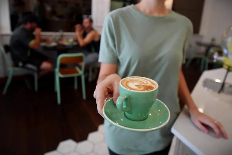 A waitress is seen holding up a coffee in a green mug.