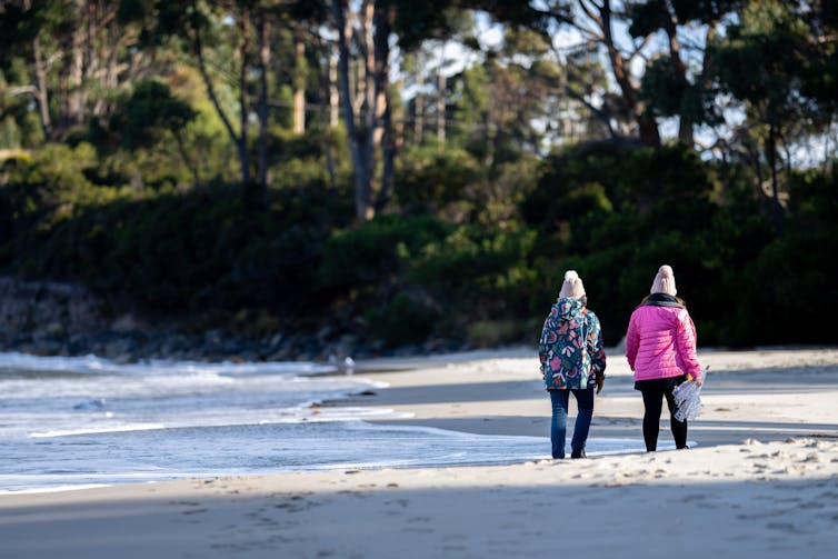 two people walk on beach with warm clothes on